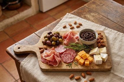 Plateau apéro rustique sur planche en bois avec charcuterie, fromages, olives et amandes disposés de façon naturelle sur une table en lin